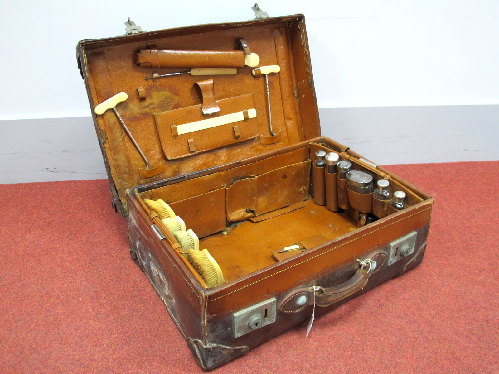 An Early XX Century Leather Bound Suitcase, the interior fitted with four ivorine backed brushes,