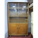 An Oak Book Cabinet, in the Ercol manner, having sliding glass upper doors over solid cupboard