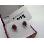 A Pair of Modern Single Stone Ruby Earstuds, each oval four claw set with diamond set highlight,