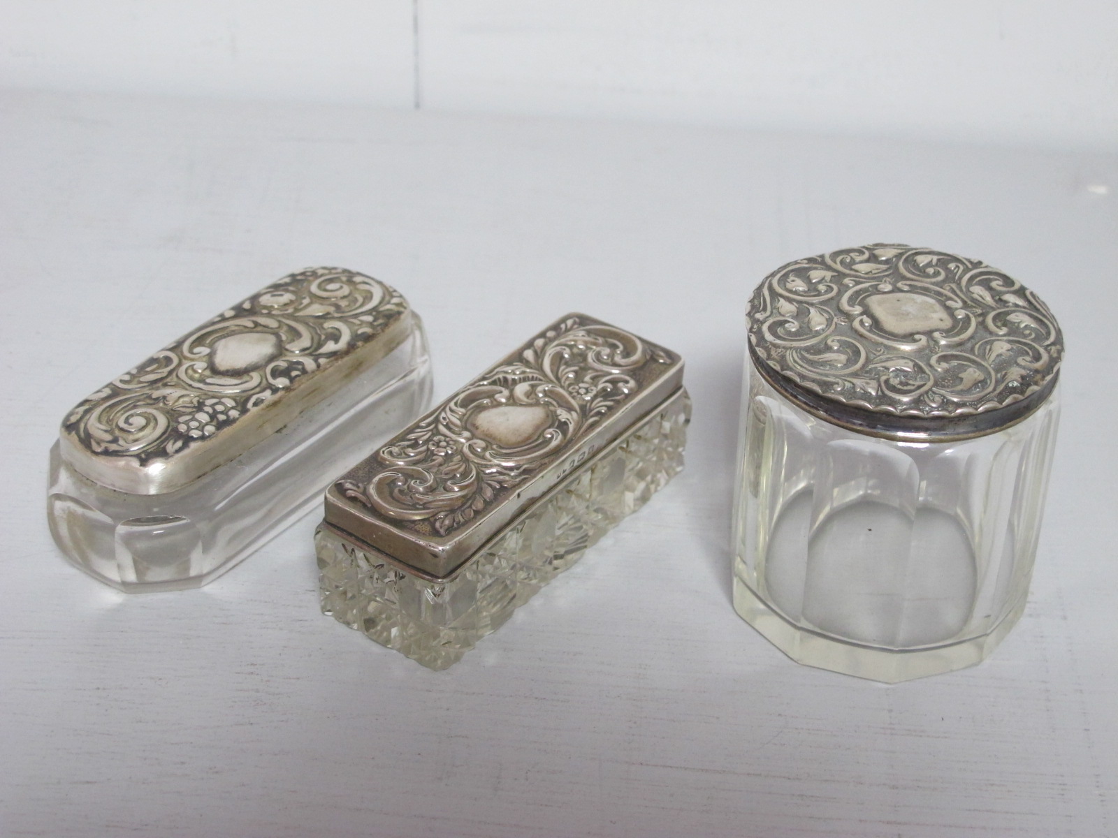 Two Hallmarked Silver Lidded Glass Dressing Table Pots, each detailed in relief with leaf scrolls;