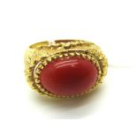 An Ornate Cabochon Set Dress Ring, within a textured border, between wide shoulders of satin finish,