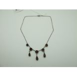 A Garnet Set Necklace, graduated circular collet set, suspending three elongated tear drops, a