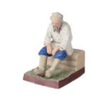 A RUSSIAN PORCELAIN FIGURE OF AN OLD MAN ON A IZBA BENCH, GARDNER PORCELAIN FACTORY, MOSCOW