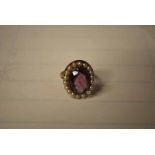 9CT GOLD DRESS RING WITH OVAL AMETHYST TYPE STONE WITHIN A BORDER OF SEED PEARLS 5.7G