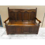 An early 19th century oak Box Settle, four panel back downswept arms with turned front supports,