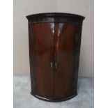 A Georgian mahogany two door wall hanging Corner Cabinet, bow front with blind fretwork frieze below