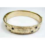 A rolled gold bangle with engraved decoration inset garnets