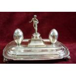 A silver novelty rugby themed inkstand with rugby player to centre flanked by two rugby ball