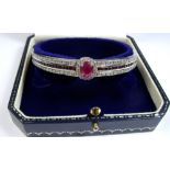 A 9 carat white gold ruby and diamond set hinged bangle with central ruby and diamond cluster set on