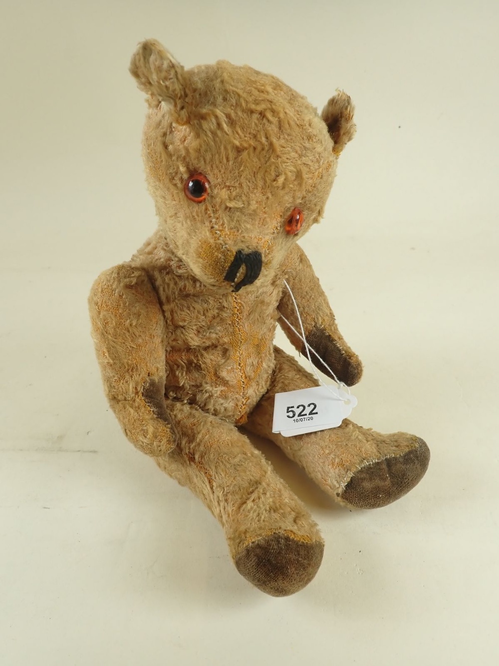 An early 20th century gold plush jointed teddy bear with glass eyes, velvet paws and stitched