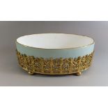 A Halcyon Days porcelain shallow oval bowl set in a gilt metal support of pierced and embossed