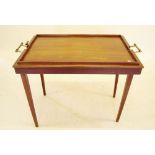 An early 20th century mahogany butlers tray with integral folding legs and brass handles, one