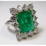 A large 18ct white gold emerald and diamond ring, the central emerald approx 6 cts within fifteen