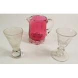 A cranberry glass cream jug and two 19th century small glasses, one engraved cow in Alpine scene