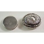 A silver oval trinket box, embossed scrollwork and a white metal circular pill or snuff box, 5 cm