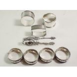 Seven various silver napkin rings, 59 gm and a pair of silver plated tongs