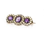 A trilogy of amethyst circular cut stones, surrounded by seed pearls on a yellow metal mount and