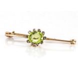 A peridot and diamond bar brooch, the oval peridot surrounded by rough cut diamonds in gold collet