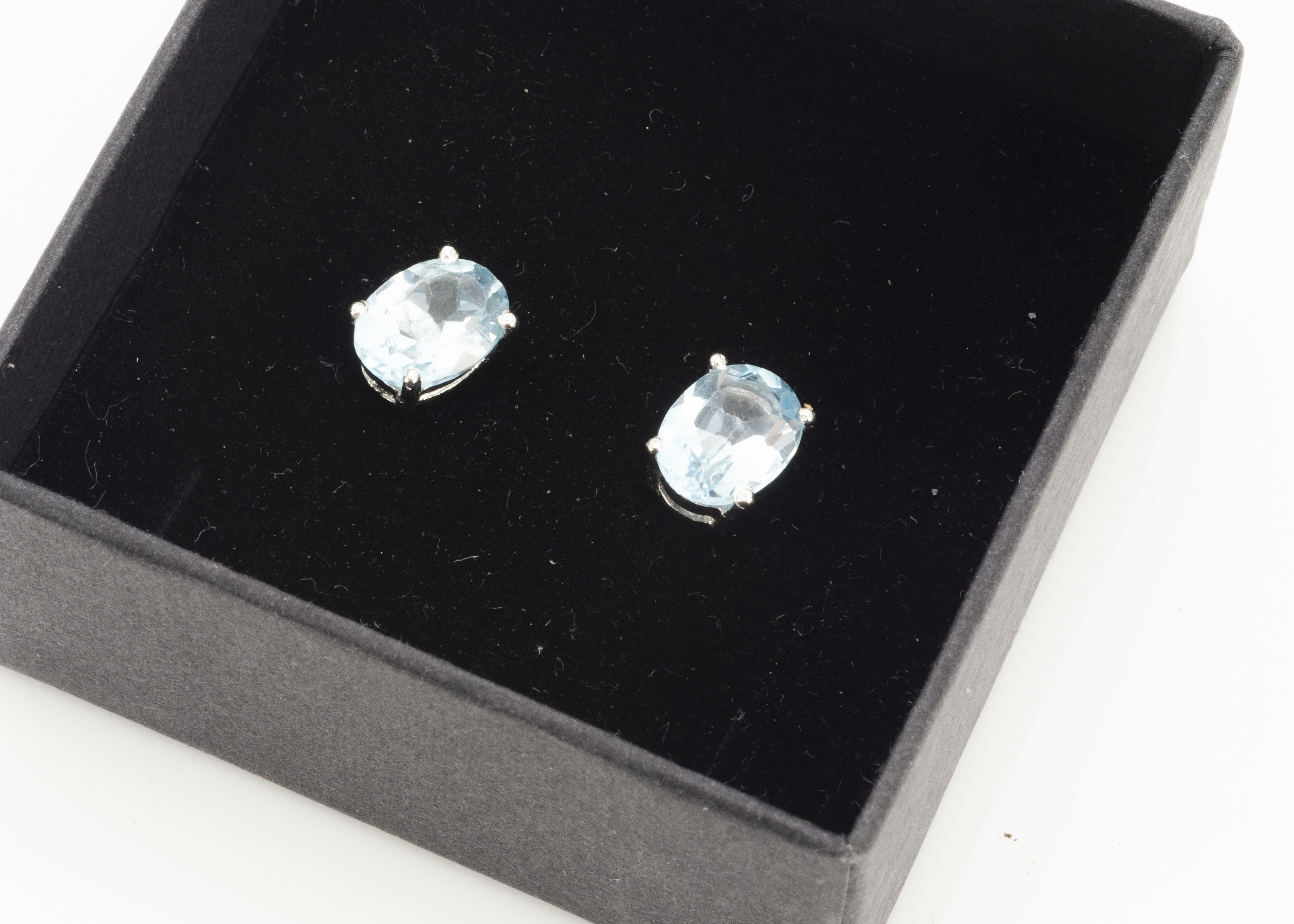 A pair of oval topaz ear studs, the light blue oval mixed cuts in four claw setting, boxed