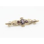 A 9ct gold garnet set bar brooch, the central oval mixed cut in claw setting flanked by two round