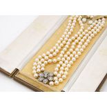 A three strand uniform cultured pearl necklace, with ornate diamond floral clasp, the knotted strung