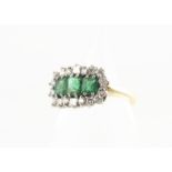 An emerald and diamond 18ct gold dress ring, the three emerald cuts in claw settings surrounded by a