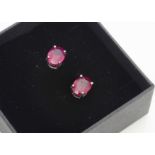 A pair of treated ruby ear studs, oval mixed cut in silver four claw setting, boxed