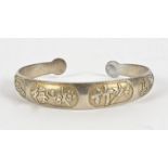 A Chinese silver bangle, decorated with flowers, bamboo, a horse, and calligraphic symbols, widest