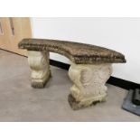 A stone garden bench of arched form, the curved seat raised upon two scrolling base plinths,