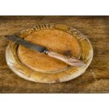 A carved wood ‘Spare Not’ bread board, —11½in. (29cm.) diameter; and a steel-bladed bread knife with