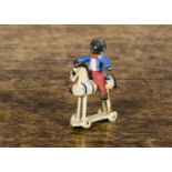 A cold-painted bronze Golliwog riding a wooden horse, on dummy wheels —1½in. (4cm.) high (missing