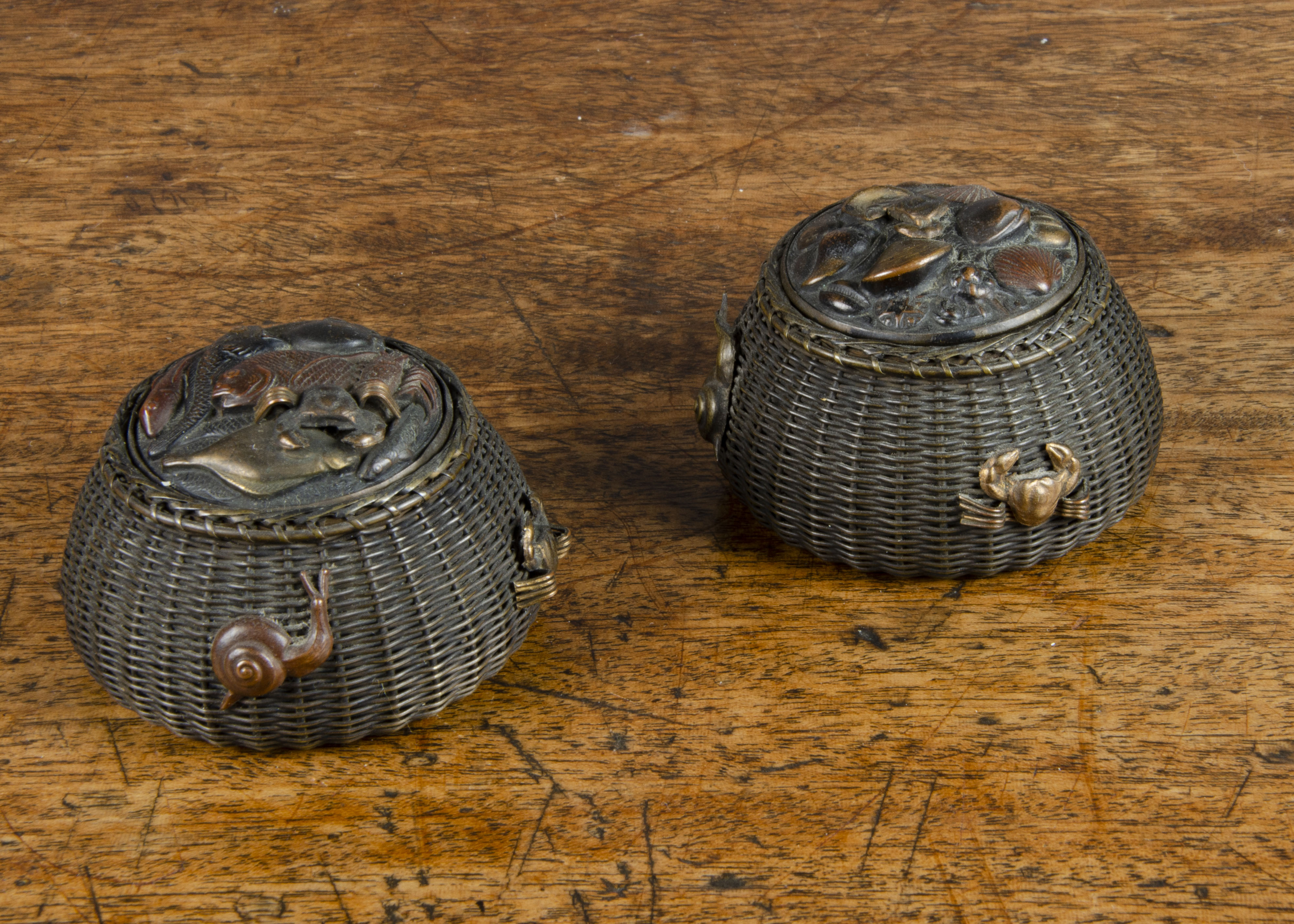 A pair of Japanese bronze fishing basket ink wells, with woven sides, the lids with assorted fish