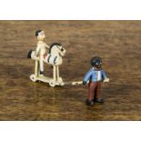 A cold-painted bronze Golliwog and Dutch doll, the Golly pulling the doll on a wooden horse on dummy