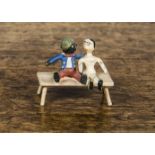 A cold-painted bronze Golliwog and Dutch doll seated on a bench, with painted wood grain —1¼in. (