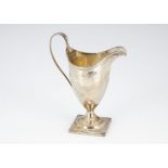 A George III style white metal milk jug, helmet shaped with loop handle on square foot, repaired