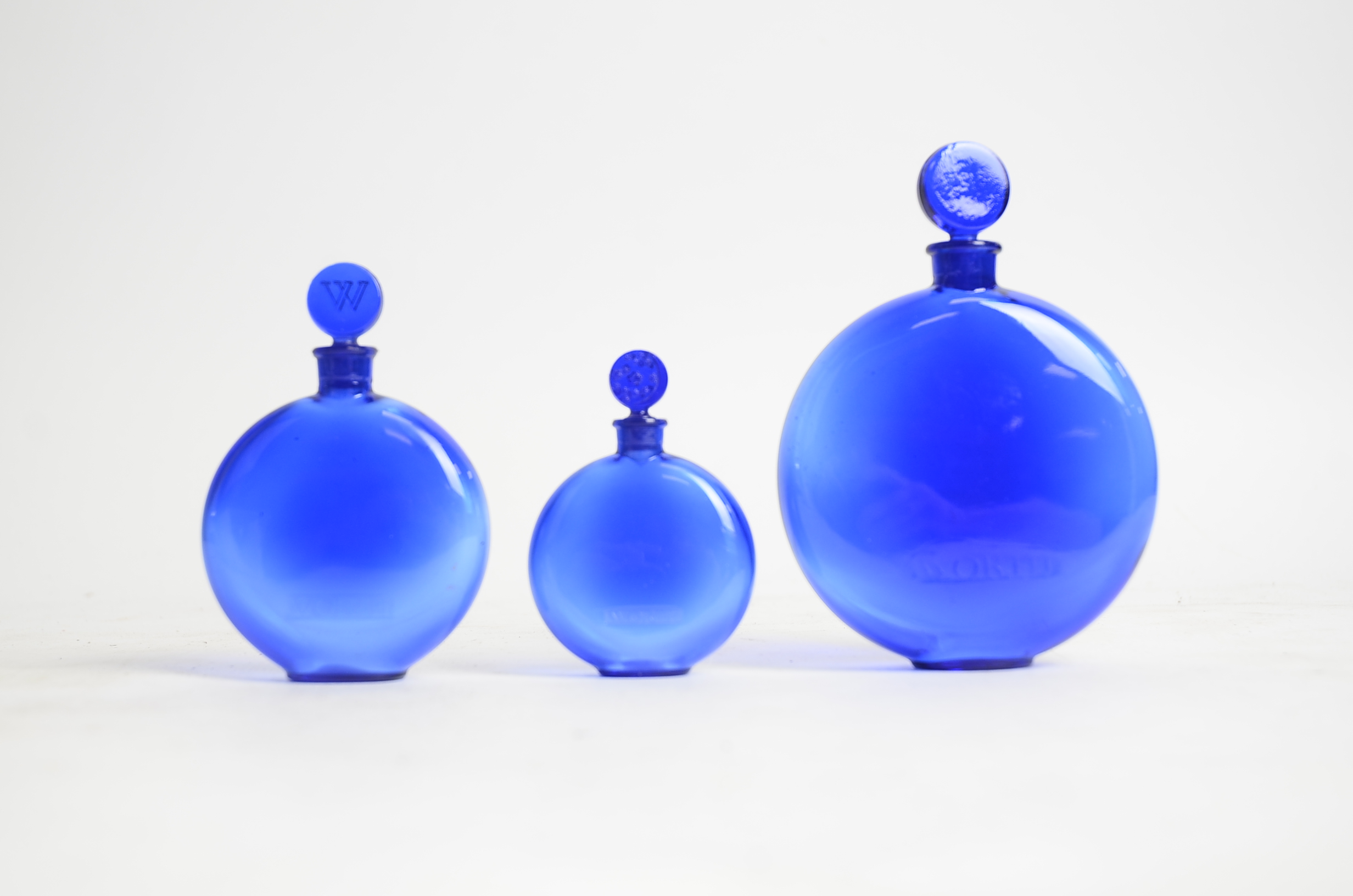 René Lalique (French, 1860-1945) a graduated set of three blue glass circular Worth perfume bottles,