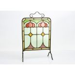 An Arts & Crafts stained glass fire screen, the brass frame with astragal glazed central