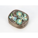 A white metal and enamel oval box, the hinged lid with embossed floral design of a lily in green and