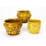 Three British pottery ochre coloured moulded jardinieres, including a stylised flower head on a