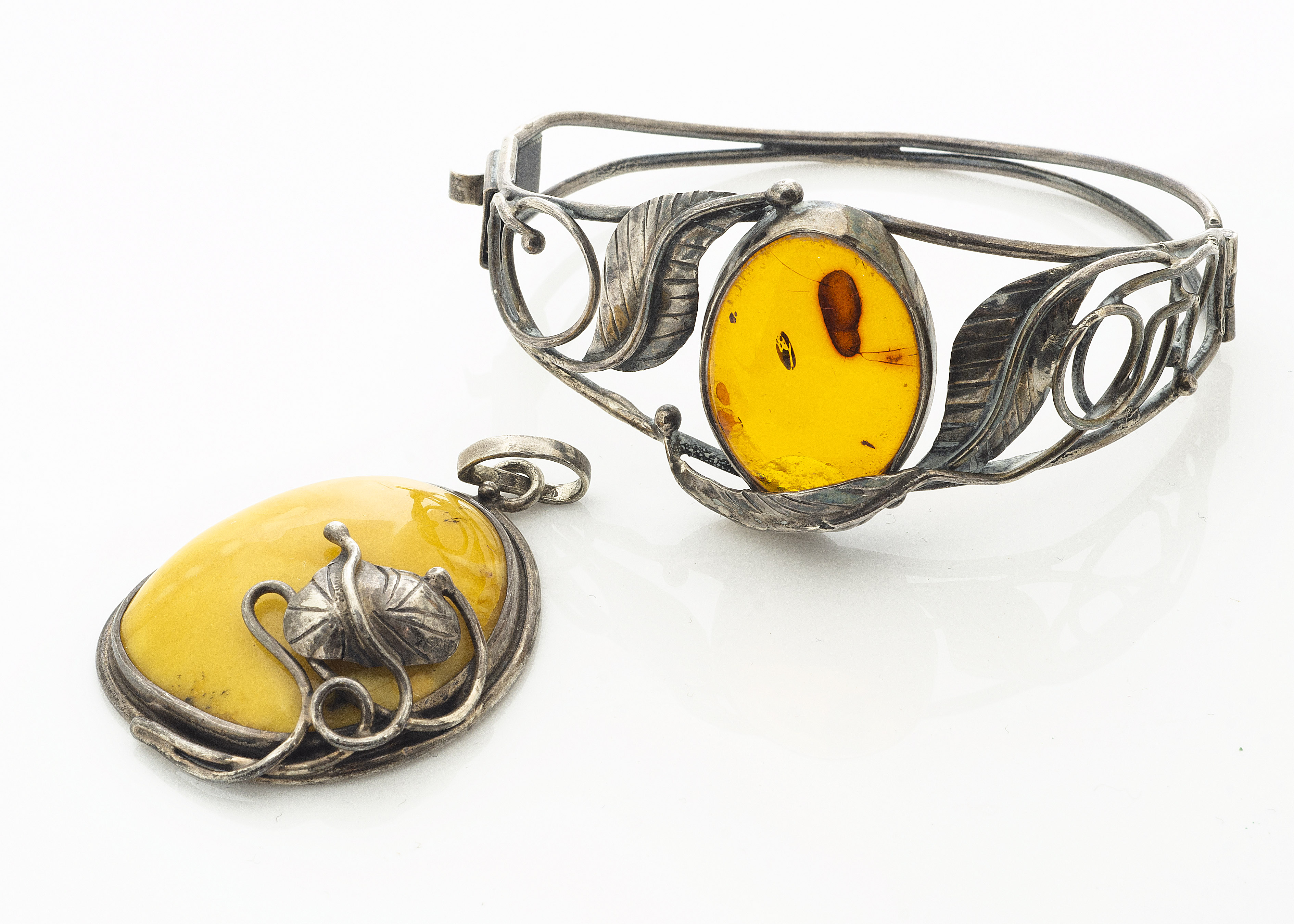 A contemporary Baltic amber bangle, the oval cabochon in pierced white metal leaf setting marked