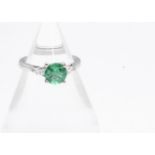 A contemporary emerald and diamond 18ct white gold three stone ring, the circular cut emerald in