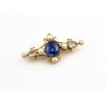 A gold synthetic sapphire and seed pearl bar brooch, the central blue claw set sapphire in a