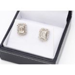 A pair of 18k white gold emerald cut diamond and brilliant cut ear studs, the central stones with