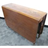 An antique mahogany drop flap table, rounded corners, raised on turned supports, finished on brass