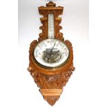An early 20th Century oak carved cased barometer, the enamel dials with red and black lettering,