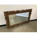 An antique carved pine frame, having rococo style scrolling foliage, inset with a glass mirror,