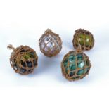 Four dumpy glass floats entwined in fishing ropes, three green, one a mauve / smoky grey hue,