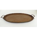 A twin handled oval copper tray, the cavetto with hammered Arts & Crafts effect, with a rope twist