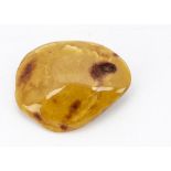 An amber pebble brooch, of natural curved ovoid form, in butterscotch and base metal applied pin,