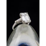 A fine certificated diamond three stone ring, the large emerald cut diamond in four claws flanked by